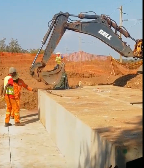 Excavator and workers beside a concrete structure on a civil construction site
